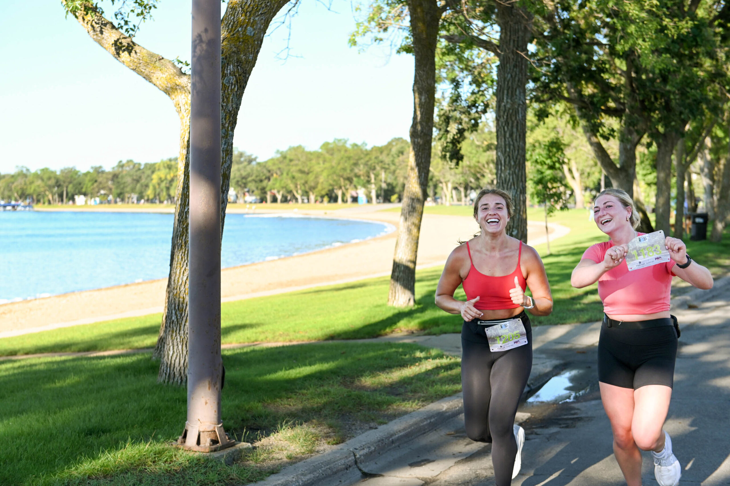 Two happy female runners • the female on the right, holds up her racing bib